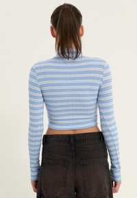 Slim-fit, langermet, kort topp i lyseblått med hvite striper, ribbet tekstur; kombinert med høyt liv svarte bukser med store lommer.