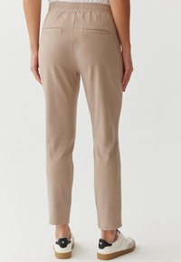 Lichtbeige joggingsbroek met een elastische tailleband en twee achterzakken. Gekocht met witte sneakers met zwarte accenten. Soepele stofstructuur.