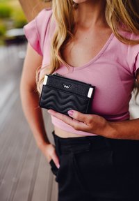 Black textured wallet with zigzag pattern, silver hardware, and zipper. Held in hand, featuring a small logo on the front.