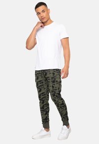 Hvid T-shirt med korte ærmer kombineret med grønne camo cargo bukser med ribbede manchetter og sidelommer. Hvide sneakers fuldender outfittet.
