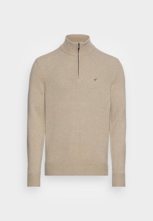 Beige knit sweater with a high collar and half-zip closure. Features ribbed cuffs and hem, with a logo embroidered on the chest.