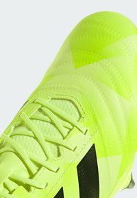 Crampons de football néon jaune vif avec une tige texturée ornée de motifs géométriques, des accents noirs et un système de laçage traditionnel pour un maintien sécurisé.