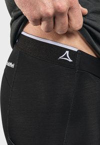 Schwarze Sportshorts mit einem breiten, strukturierten elastischen Bund, der ein weißes Logo zeigt. Eine Nahaufnahme zeigt die Nähdetails und Passform.