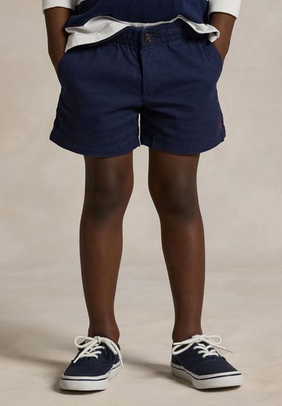 Calções de algodão azul-marinho com cintura elástica e bolsos laterais; combinados com ténis escuros com atacadores brancos e sola texturizada.