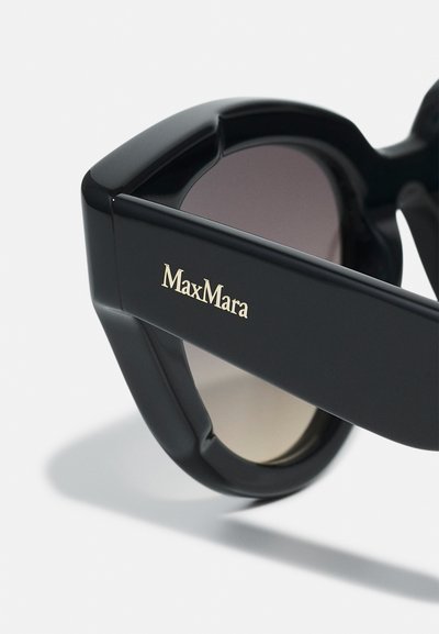 Black plastic sunglasses feature a bold geometric design with ombre lenses and a gold "MaxMara" logo on the temple.