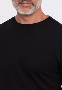 Musta puuvillapaita, jossa on pyöreä pääntie, lyhyet hihat ja sileä rakenne. Varustettu olkakoristeilla lisäyksien vuoksi.