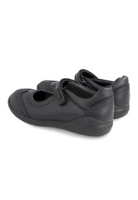 Zapatos de cuero negro con puntera redondeada, detalles de brogue y una correa de Velcro. Presentan una suela de goma texturizada y un interior suave.