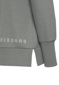 Felpa grigia con polsini e orlo a costine, caratterizzata da uno spacco laterale. Tessuto texturizzato e un logo bianco ben visibile sulla parte anteriore inferiore.