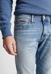 Ljusblå denimjeans med en lätt blekt finish, med en enkel bakficka med röd kontrastsöm och en metallknapp i midjan.