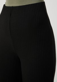 Černé žebrované kalhoty s designem s vysokým pasem, svislou strukturou a hladkým povrchem. Bez viditelných kovových doplňků nebo akcentů.