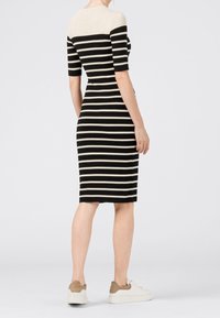 Robe ajustée jusqu'aux genoux en rayures horizontales noires et crème, à manches courtes, col rond, en tissu doux. Associée à des baskets blanches.