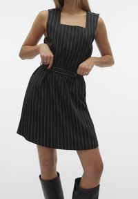 Robe noire à rayures verticales avec un décolleté carré, sans manches, taille cintrée et une ceinture en tissu. Texture lisse et coupe à hauteur des genoux.