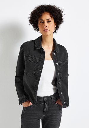 Svart denimjacka med klassisk krage, framknäppning och två bröstfickor. Bärs över en vit tanktop med matchande svarta jeans.