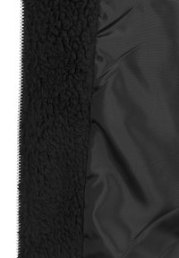 Interior de chaqueta negra que muestra un forro suave de felpa en un lado y una tela lisa con una cremallera visible en el otro.