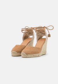 Espadrillas con zeppa in suede color beige, con suola in juta intrecciata e apertura sul retro. I lacci alla caviglia presentano un ciondolo decorativo. Tessuto liscio.
