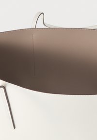 Λευκή δερμάτινη τσάντα tote με απαλή υφή και μίνιμαλ σχεδιασμό. Εσωτερικό σε απαλό μπεζ χρώμα, χωρίς ορατά μεταλλικά μέρη ή θήκες.