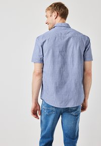 Kurzarmhemd in Blau- und Weißstreifen mit Button-Down-Kragen, ausgestattet mit geradem Saum und Rückenpasse, kombiniert mit hellblauen Jeans.