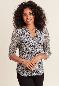 Schwarz-weiße Bluse mit Blumendruck, V-Ausschnitt, Dreiviertelärmeln und leichtem, transparentem Stoff. Tragen mit schwarzen Hosen.