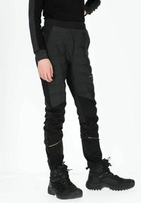 Zwarte geïsoleerde broek met een gewatteerde textuur en taps toelopende benen, gecombineerd met robuuste zwarte outdoor boots. Bevat gouden accenten en een gladde tailleband.