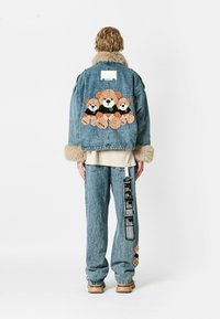 Chaqueta de denim con cuello de piel sintética, que presenta un motivo de oso en tonos tierra en la espalda. Pantalones de denim de corte relajado con una etiqueta en el lateral.