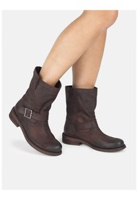 Botas de cuero marrón hasta el tobillo con un diseño arrugado, correa ajustable y acentos de hebilla plateada, tacón bajo apilado y superficie texturizada.