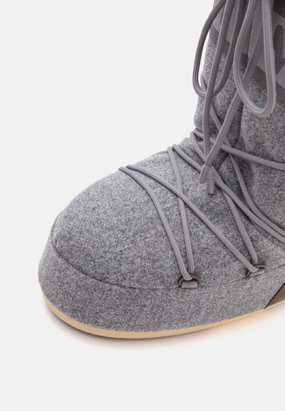 Gros plan d’une botte d’hiver en feutre gris avec une semelle beige et des lacets gris croisés attachés par des œillets métalliques.