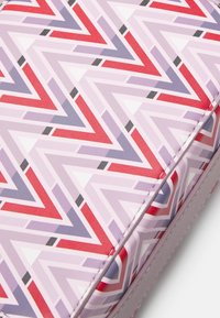 Detailní záběr na látku se zigzag vzorem v červené, levandulové, šedé a bílé barvě se viditelným stehem podél okraje.