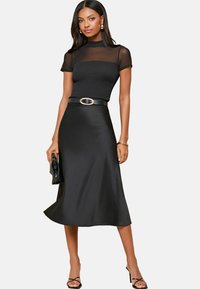 Robe midi noire avec un corsage ajusté et des manches courtes transparentes, cintrée à la taille avec une ceinture noire. Tissu lisse avec une légère brillance.