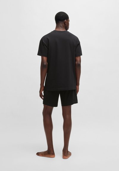 T-shirt en coton noir à manches courtes, associé à un short noir. Design simple, coupe décontractée, et sans motifs ni accents visibles.