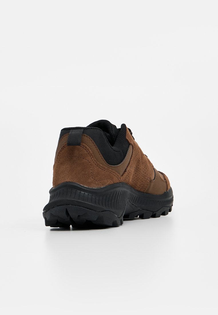 Zapatillas deportivas de ante marrón y malla negra con una suela de goma negra rugosa y acentos texturizados, con un collar acolchado y una etiqueta en el talón.