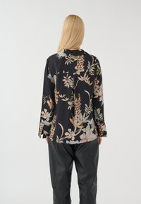 Bluse mit floralen Druck in Schwarz, ausgestattet mit langen Ärmeln und einem leichten High-Low-Saum. Verziert mit pastellfarbenen Blumen und Blättern.