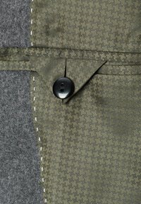 Texturiert olivgrüner Stoff mit Hahnentrittmuster, versehen mit einem schwarzen Knopf und kontrastierendem grauen Filz auf der linken Seite.