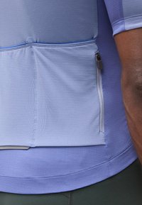 Κοντινό πλάνο ενός ατόμου που φοράει ένα ανοιχτό μπλε υφασμάτινο ποδηλατικό τζέρσεϊ με φερμουάρ στην πίσω τσέπη και κοντά μανίκια.