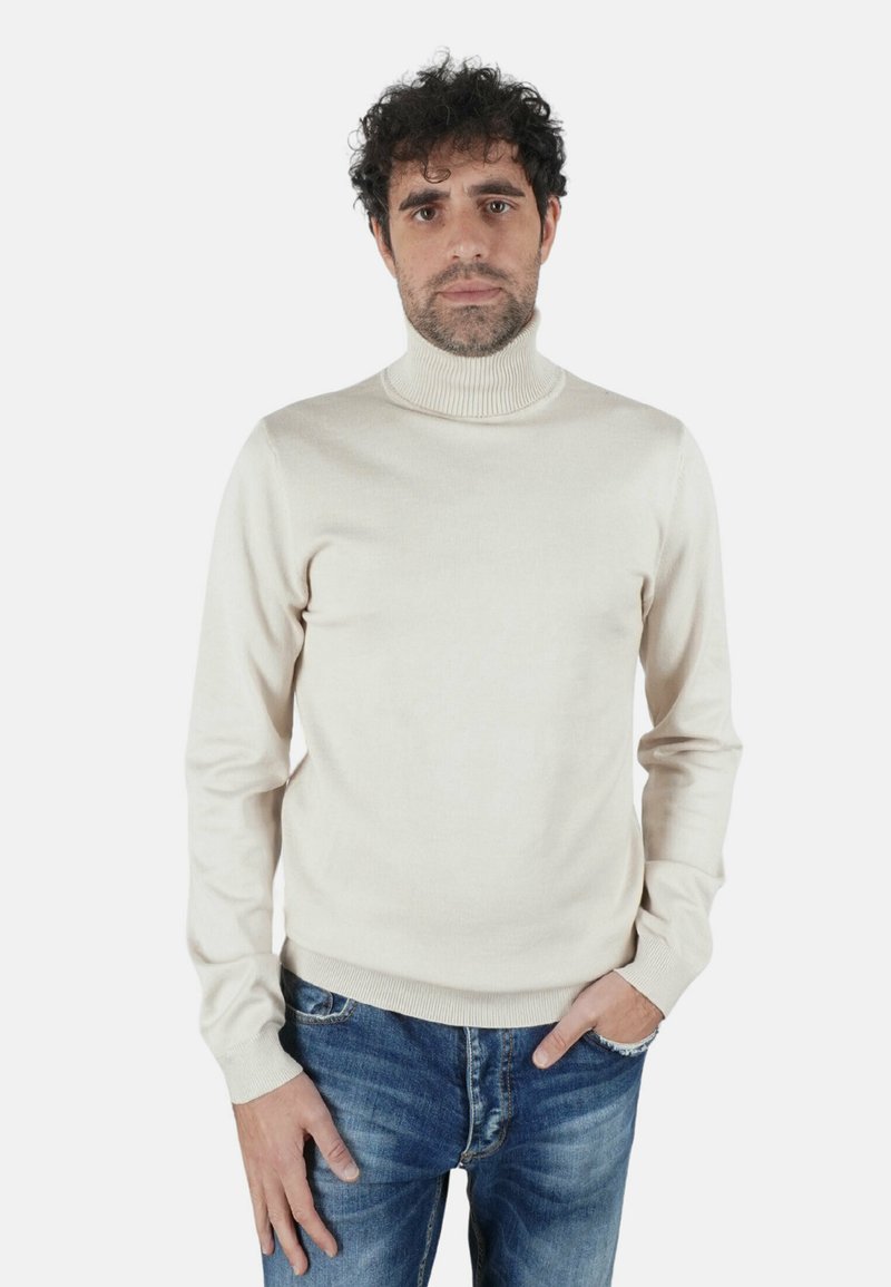 Maglione beige chiaro a collo alto in tessuto morbido, design aderente con collo e polsini a coste, abbinato a jeans di denim blu.