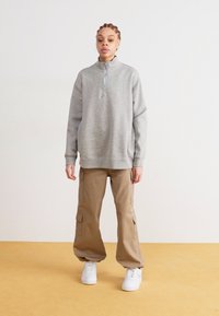 Grå hettegenser med glidelås i halsen, sammen med beige cargobukser med sidelommer, og hvite joggesko. Enkelt design og avslappet passform.