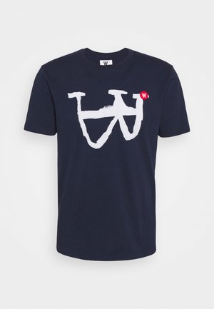 Laivastonsininen lyhythihainen T-paita, jossa suuri valkoinen abstrakti "W"-kuvio ja pieni punainen pyöreä logo oikean yläpuolen etupuolella.
