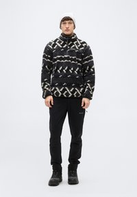 Πουλόβερ από φλις με γεωμετρικό ασπρόμαυρο σχέδιο, ψηλό γιακά, φερμουάρ, σετ με μαύρο παντελόνι εξωτερικού χώρου και ανθεκτικά παπούτσια.