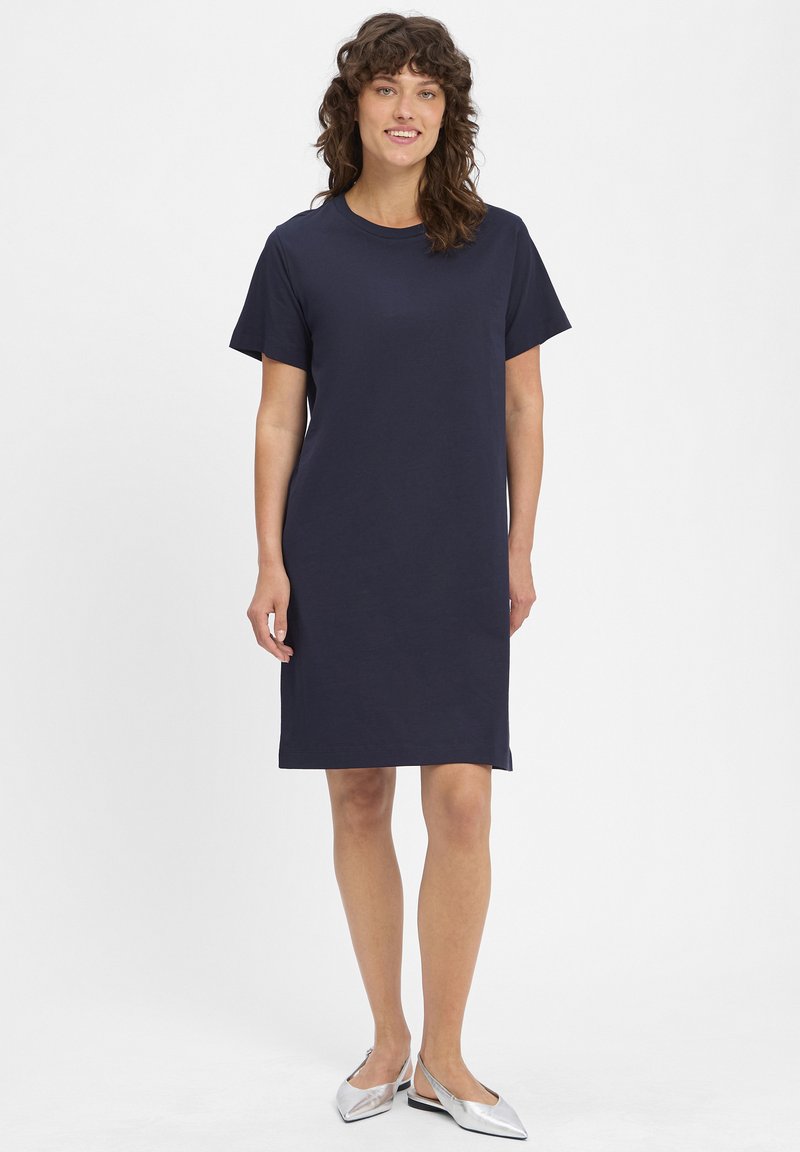 Navyblaues, kurzärmliges T-Shirt-Kleid aus Baumwolle. Einfaches Design, knielang, mit Rundhalsausschnitt und lässiger Passform. Silbergene Schuhe.