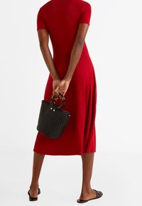 Rotes kurzärmliges Kleid mit tailliertem Oberteil und gefaltetem Rock, kombiniert mit einer kleinen schwarzen gewebten Handtasche und flachen Sandalen.