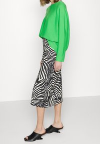 Pull court vert, jupe midi rayée noir et blanc, mules noires à talons. Le tissu semble doux ; le design présente un motif audacieux et un style superposé.