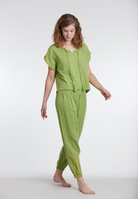 Completo verde a due pezzi realizzato in tessuto leggero. La parte superiore presenta maniche corte e scollo a V con nappine. I pantaloni sono affusolati con polsini elastici.