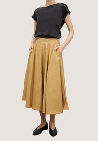 Černý saténový top s krátkým rukávem ve spojení se světle hnědou plisovanou midi sukní s jemným proužkovaným vzorem. Model má na sobě černé baleríny.