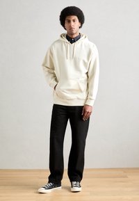 Krémová mikina s kapucí a přední kapsou, kombinovaná s černými džíny a námořnickými teniskami. Hladká tkanina a minimalistický design.