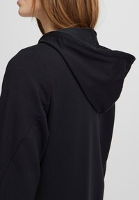Black hoodie with a soft texture, featuring a prominent hood and a relaxed fit. Design emphasizes simplicity and comfort.