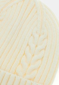 Bonnet tricoté jaune en fil doux, avec une texture côtelée et un motif en câble central. Forme arrondie, confortable et épais.