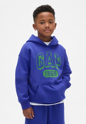 Blauwe hoodie gemaakt van zachte stof, met een groen "GAP"-logo en de tekst "1969". Voorzien van een kangoeroezak aan de voorkant en een losse pasvorm.