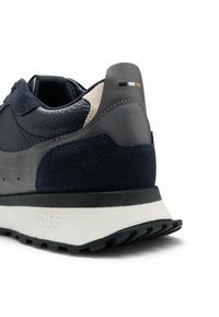 Marinblå sneakers i läder och mocka. Har en strukturerad ovandel, rund tå och en vit gummisula. Logotyp på hälen.