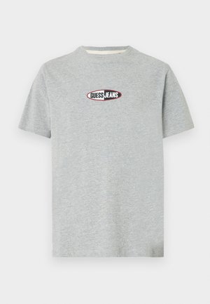 Szürke pamut rövid ujjú póló, kerek nyakkal és jellegzetes "GUESS JEANS" logóval az elején, fekete és piros színben, ovális háttéren.
