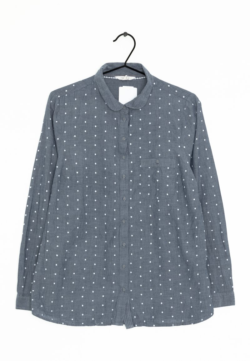 Chemise grise à manches longues avec des pois blancs, une poche poitrine et un col arrondi, suspendue sur un cintre noir.