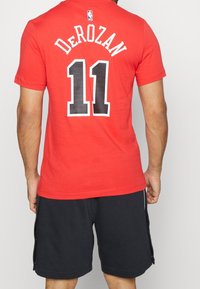 Red cotton T-shirt with black number "11" and "DeRozan" printed on the back, short sleeves, and a round neckline. Black shorts complete the outfit.